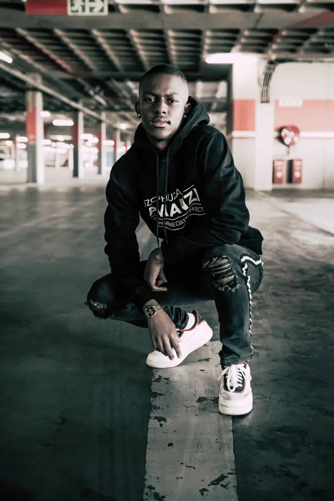 Junger Mann in schwarzem Hoodie hockt in einem Betonparkhaus