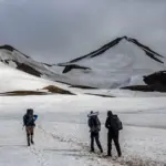 Wanderer überqueren ein Schneefeld in Richtung eines Vulkangipfels