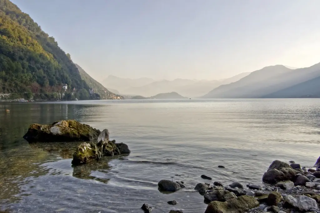 Ufer des Comer Sees mit Bergen im Morgennebel in Italien