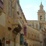 Straße mit Kalksteinhäusern und Kirchturm auf Malta