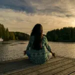 Woman meditating on a jetty by a lake