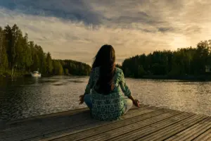 Frau meditiert auf einem Steg am See